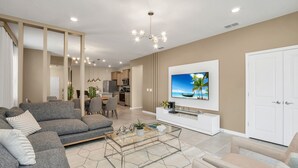 A modern living room with a grey sofa, a glass coffee table, and a flat-screen TV mounted on the wall.