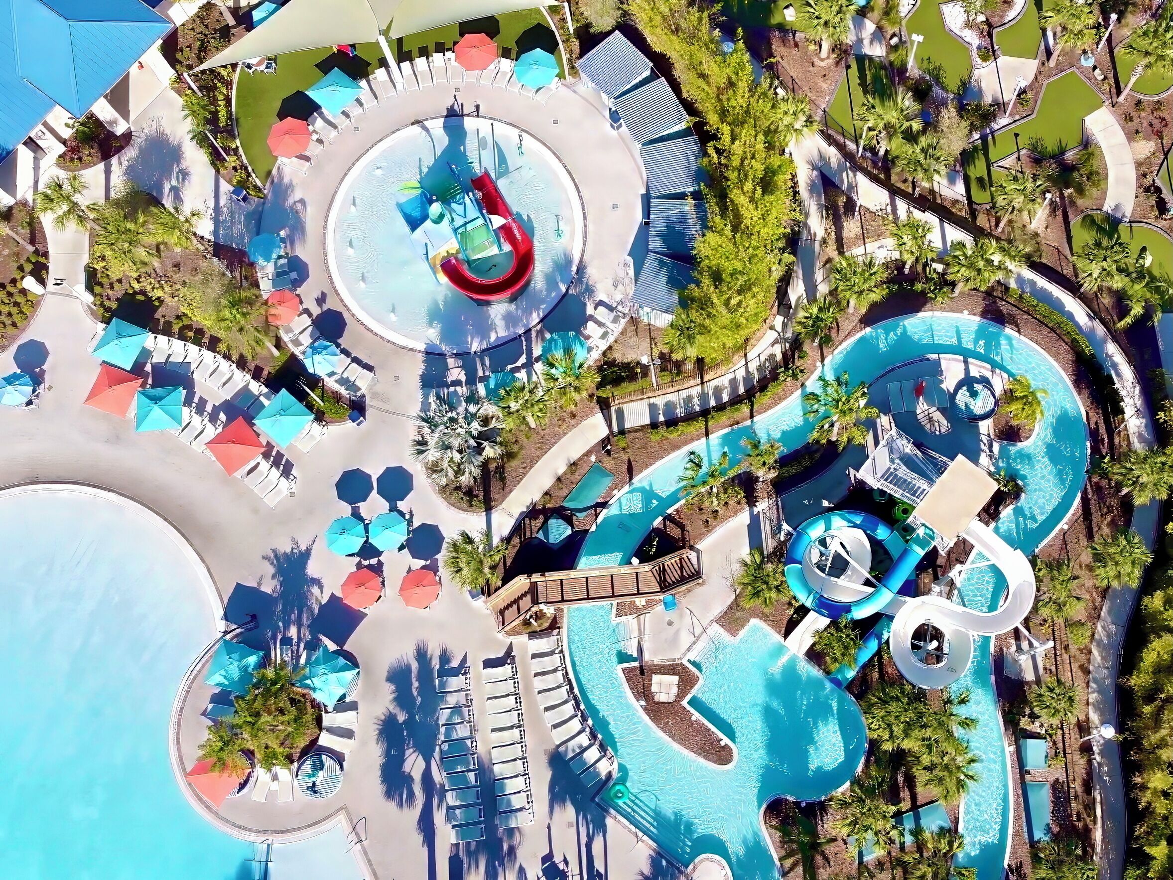 An aerial view of a resort with a large central pool, multiple smaller pools, and a water slide.