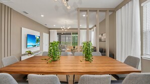 A conference room with a wooden table, grey chairs, a large TV, and a modern chandelier.