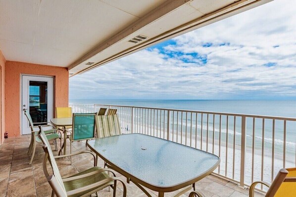 A balcony with a glass table and chairs, overlooking a beach.