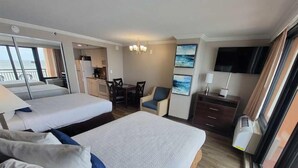Ein Hotelzimmer mit zwei Betten, einem Essbereich, einem Fernseher und Meerblick.
