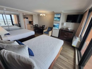 A hotel room with two beds, a dining area, a TV, and a view of the sea.