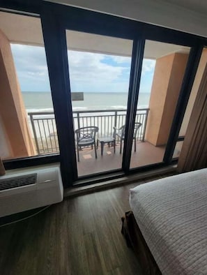 Una habitación con un ventanal grande que da a la playa, una cama y una silla.