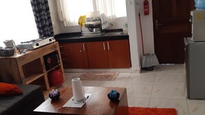 Cocina compacta con armarios de madera, una encimera con vajilla, un dispensador de agua y un refrigerador.