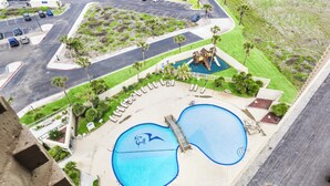 Ein Poolbereich mit zwei großen Pools, einer Kinderspielanlage und einer Sitzgelegenheit mit Liegestühlen.