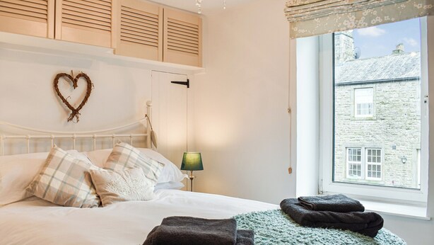 A neatly made bed with a heart-shaped decoration, a lamp, and towels on a window seat. - 2 bedroom accommodation in Clapham, near Ingleton (Clapham, near Ingleton)