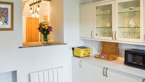 A kitchen with white cabinets, a yellow toaster, a microwave, and a glass cabinet with tea cups and glasses. - 2 bedroom accommodation in Clapham, near Ingleton (Clapham, near Ingleton)