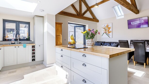 A modern kitchen with a central island, wooden beams, and a dining area with a table and chairs.