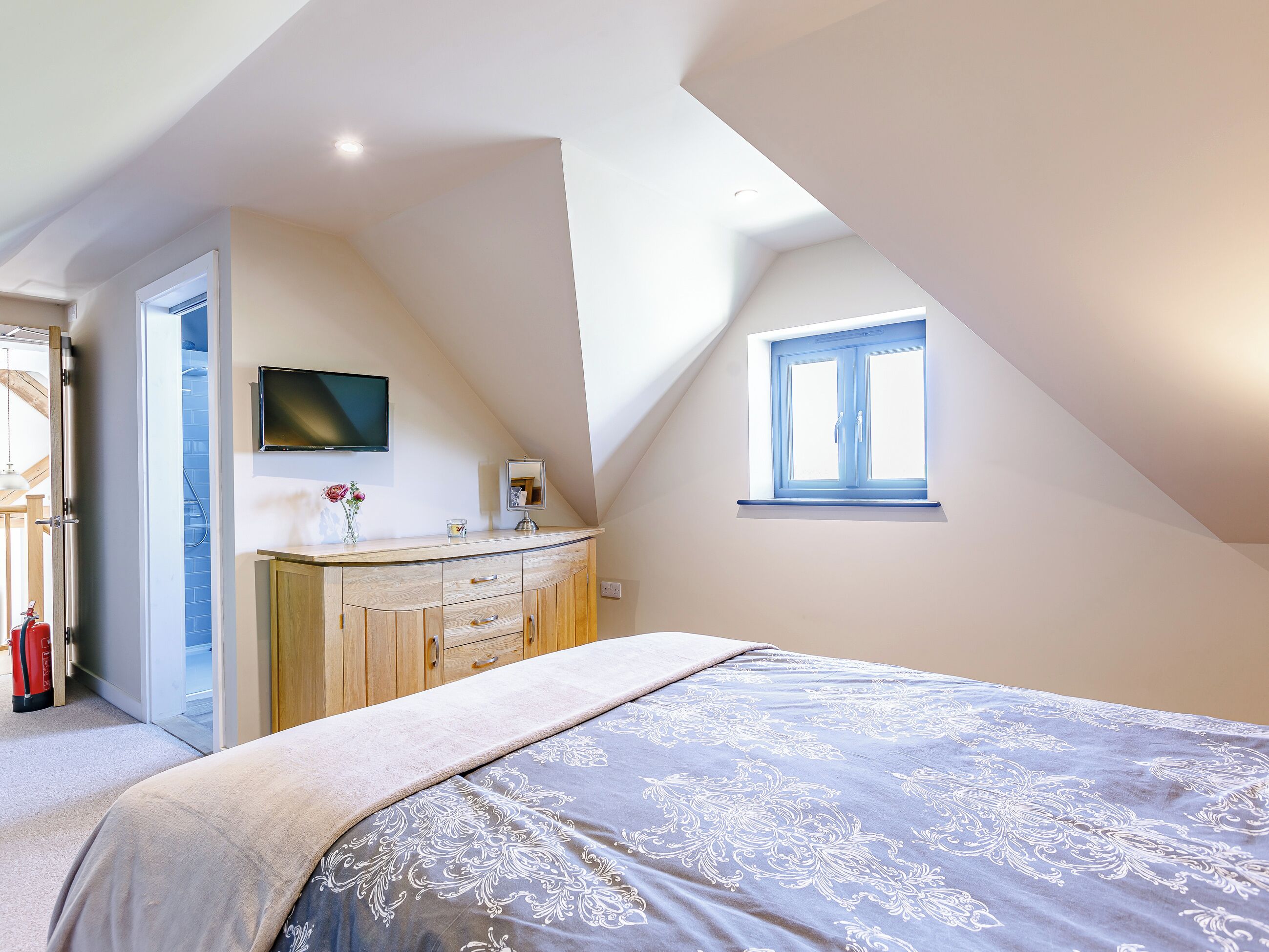 A bedroom with a bed, a TV, a window, and a door.
