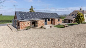 A house with a solar panel roof, a gravel driveway, and a view of the countryside.
