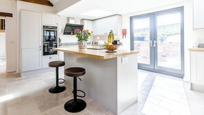 A modern kitchen with a central island, bar stools, and a view through a glass door.