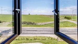 A view through an open door with a rural landscape, including fields and a road.