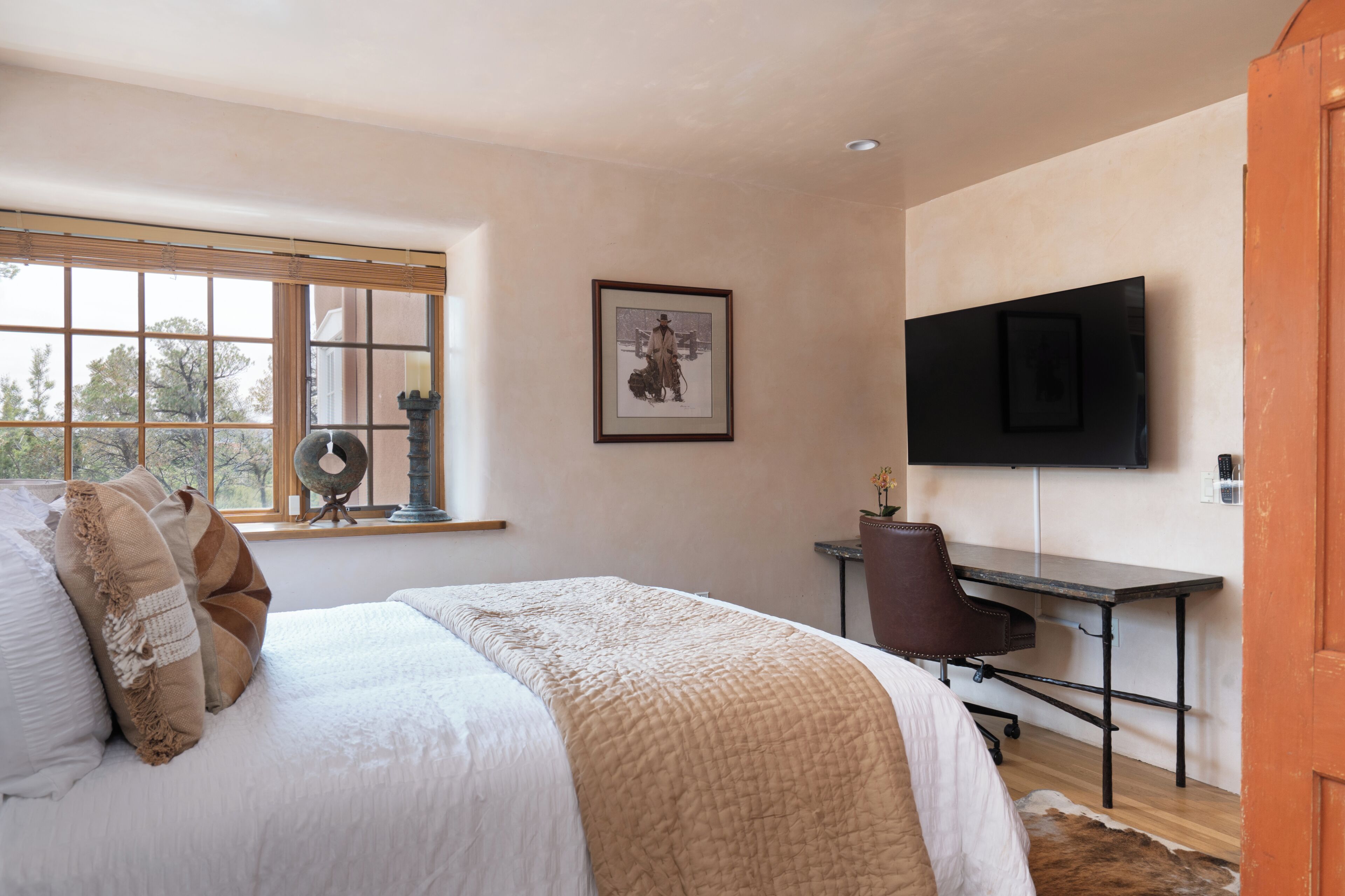 A bedroom with a bed, a desk, a chair, a television, and a window with blinds.