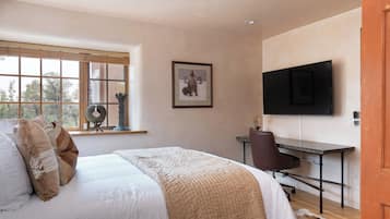 A bedroom with a bed, a desk, a chair, a television, and a window with blinds.