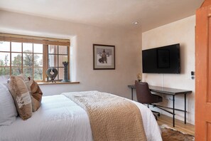 Ein Schlafzimmer mit Bett, Schreibtisch, Stuhl, Fernseher und einem Fenster mit Jalousien.