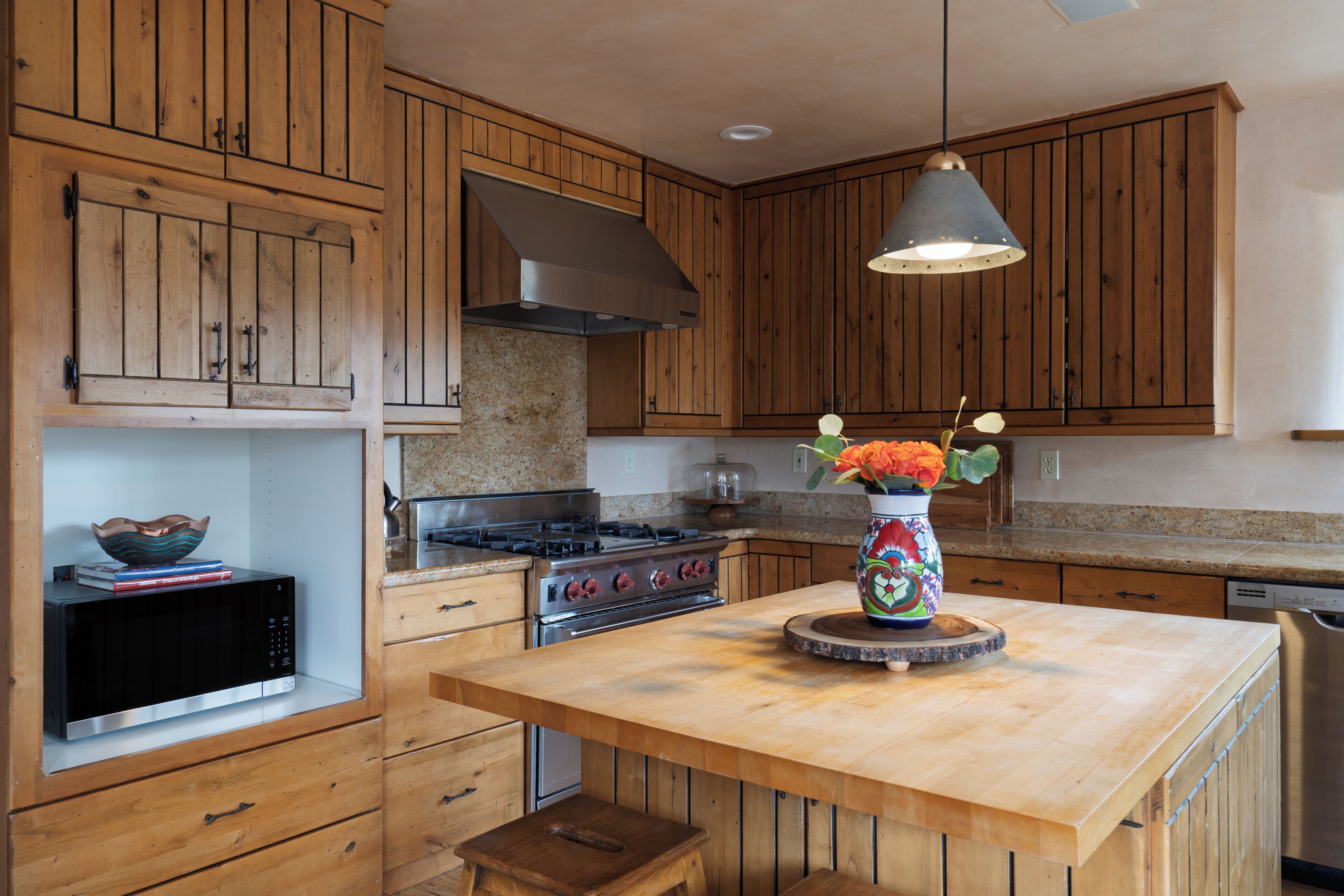 A kitchen with wooden cabinets, a stove, a microwave, a sink, and a vase with flowers on the island.