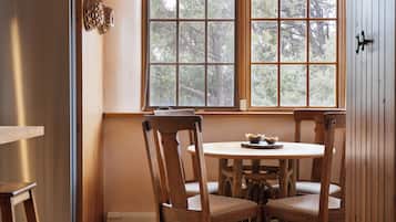 A kitchen with wooden cabinets, a refrigerator, a dining table with chairs, and a window with a view of trees.