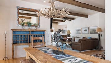 A rustic interior with a wooden dining table, a chandelier with antlers, a fireplace, and a sofa.