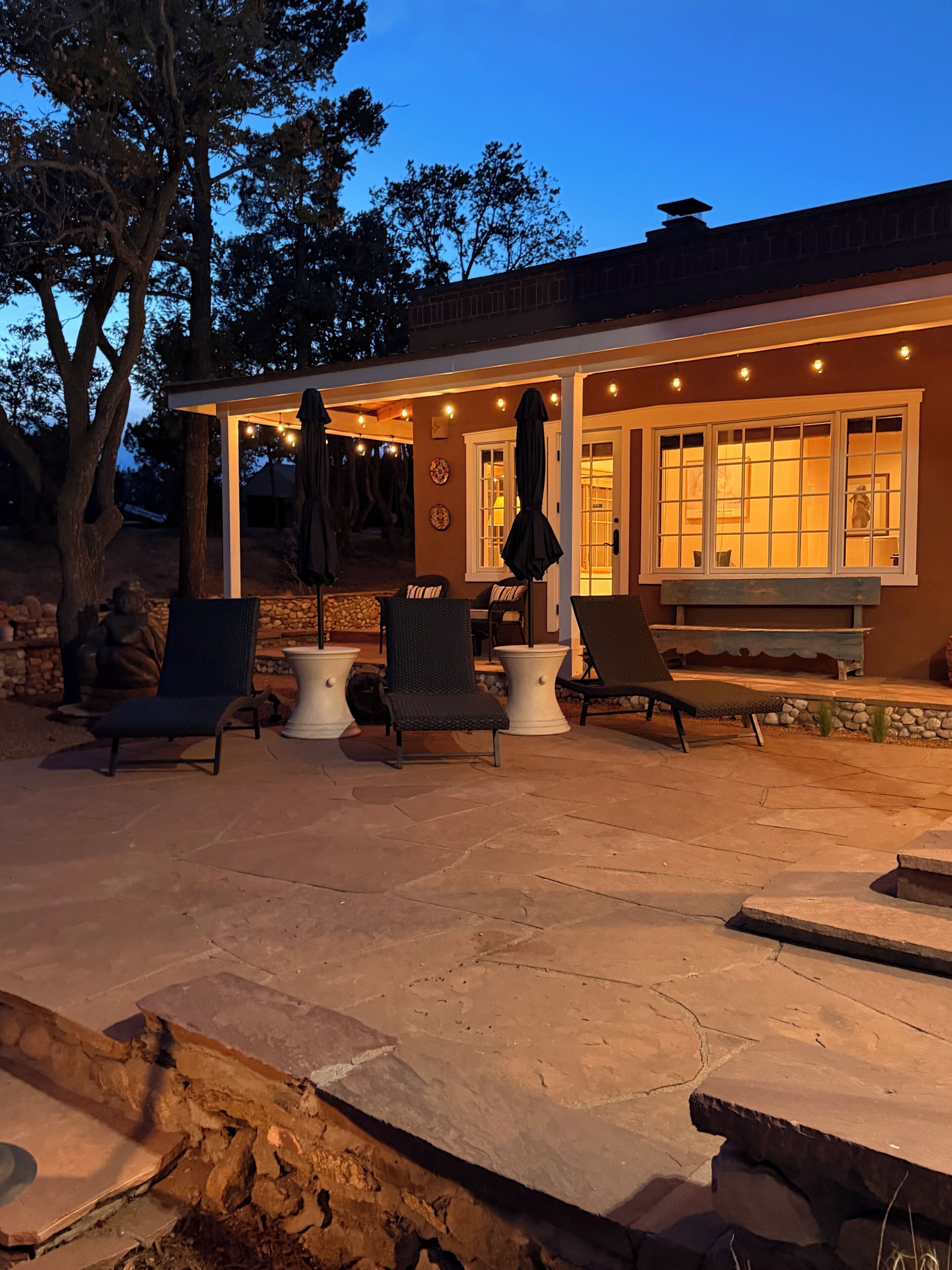 Un espace extérieur aménagé en terrasse, avec un sol en pierre, du mobilier d’extérieur et un coin salon couvert agrémenté de guirlandes lumineuses.