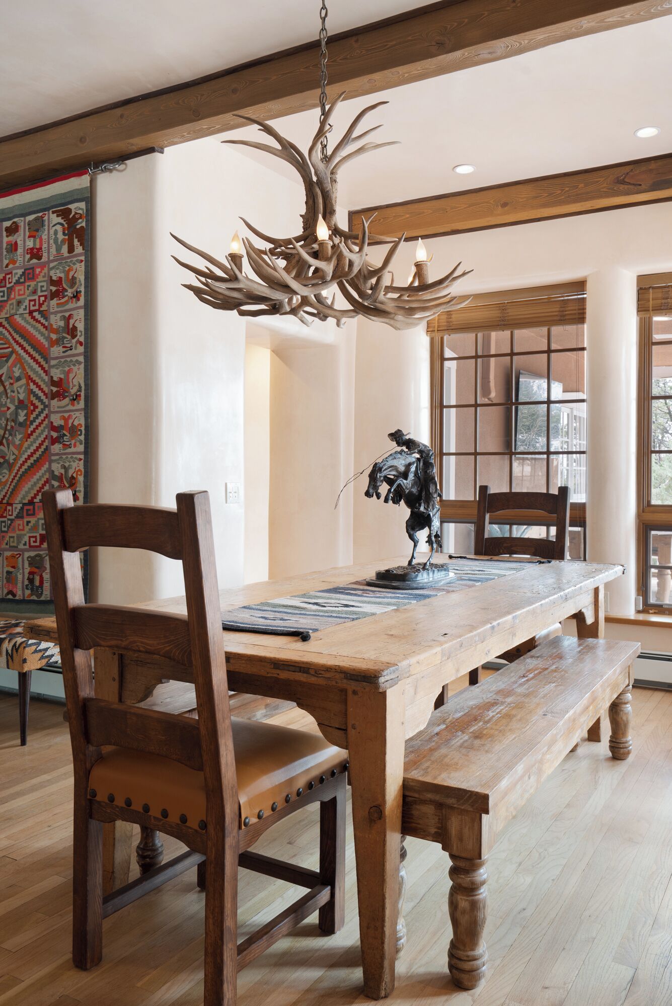 A wooden dining table with benches, a chandelier, and a horse statue.