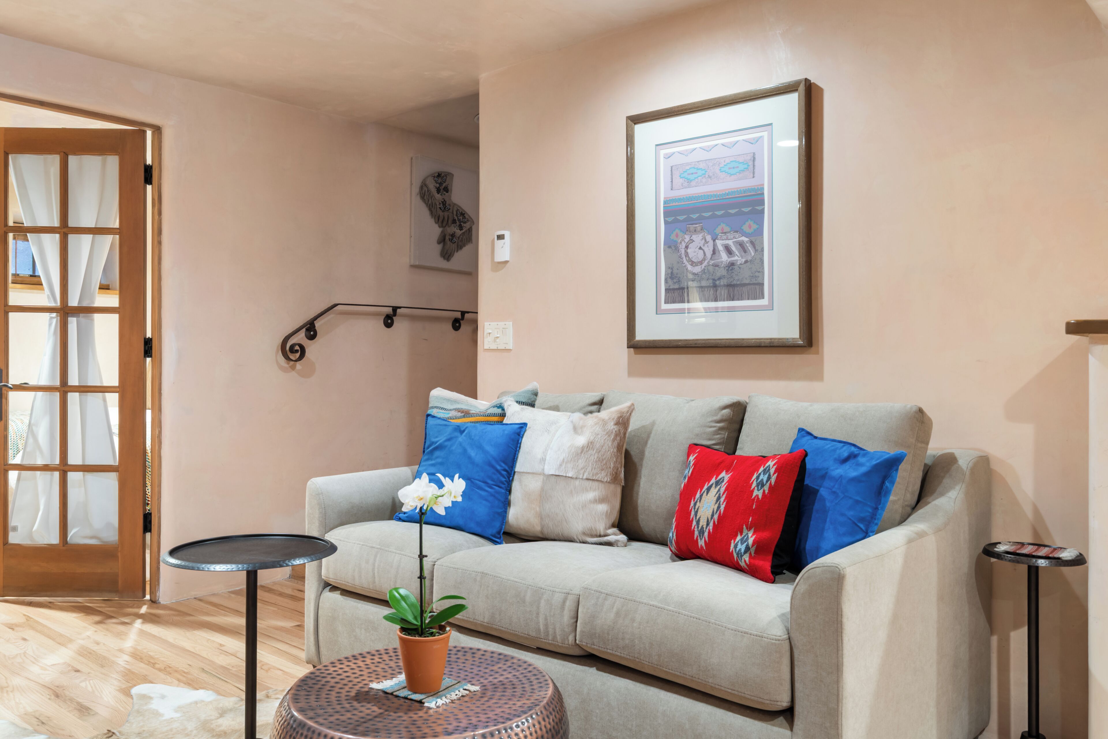 A living room with a sofa, a small round table, a potted plant, a framed picture on the wall, and a door with curtains.