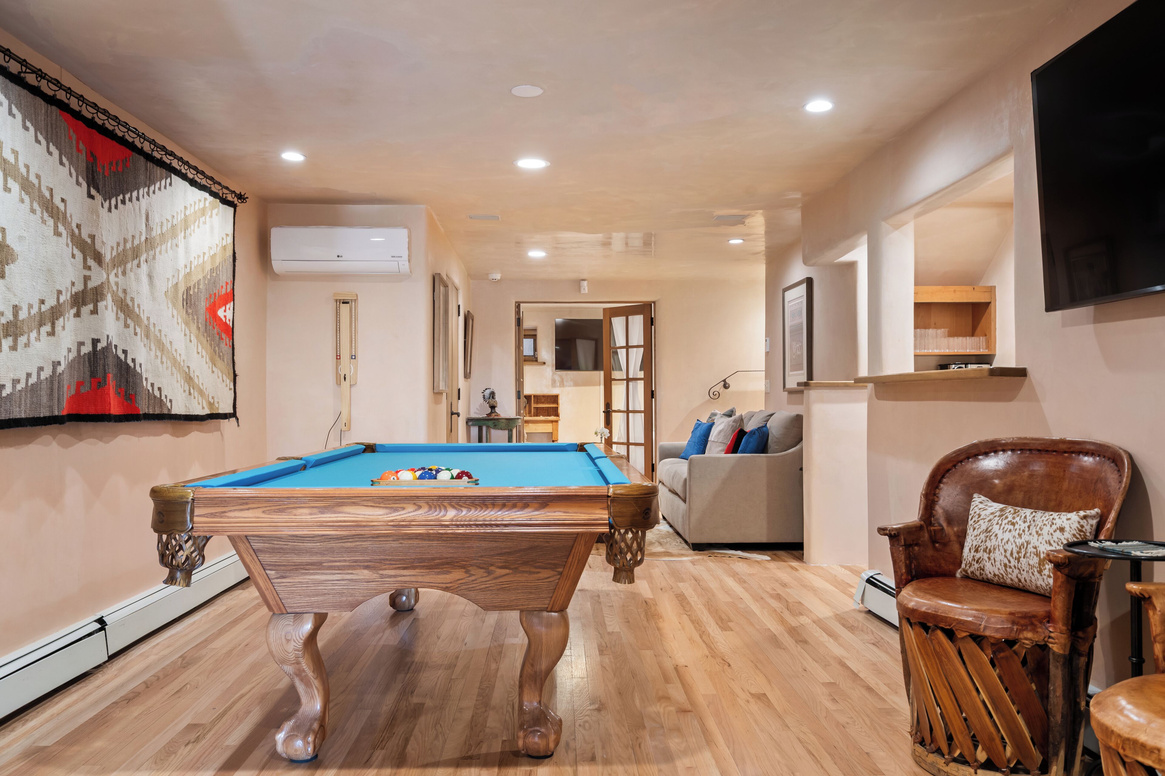 A pool table in a room with a wooden floor, a sofa, a chair, and a television mounted on the wall.