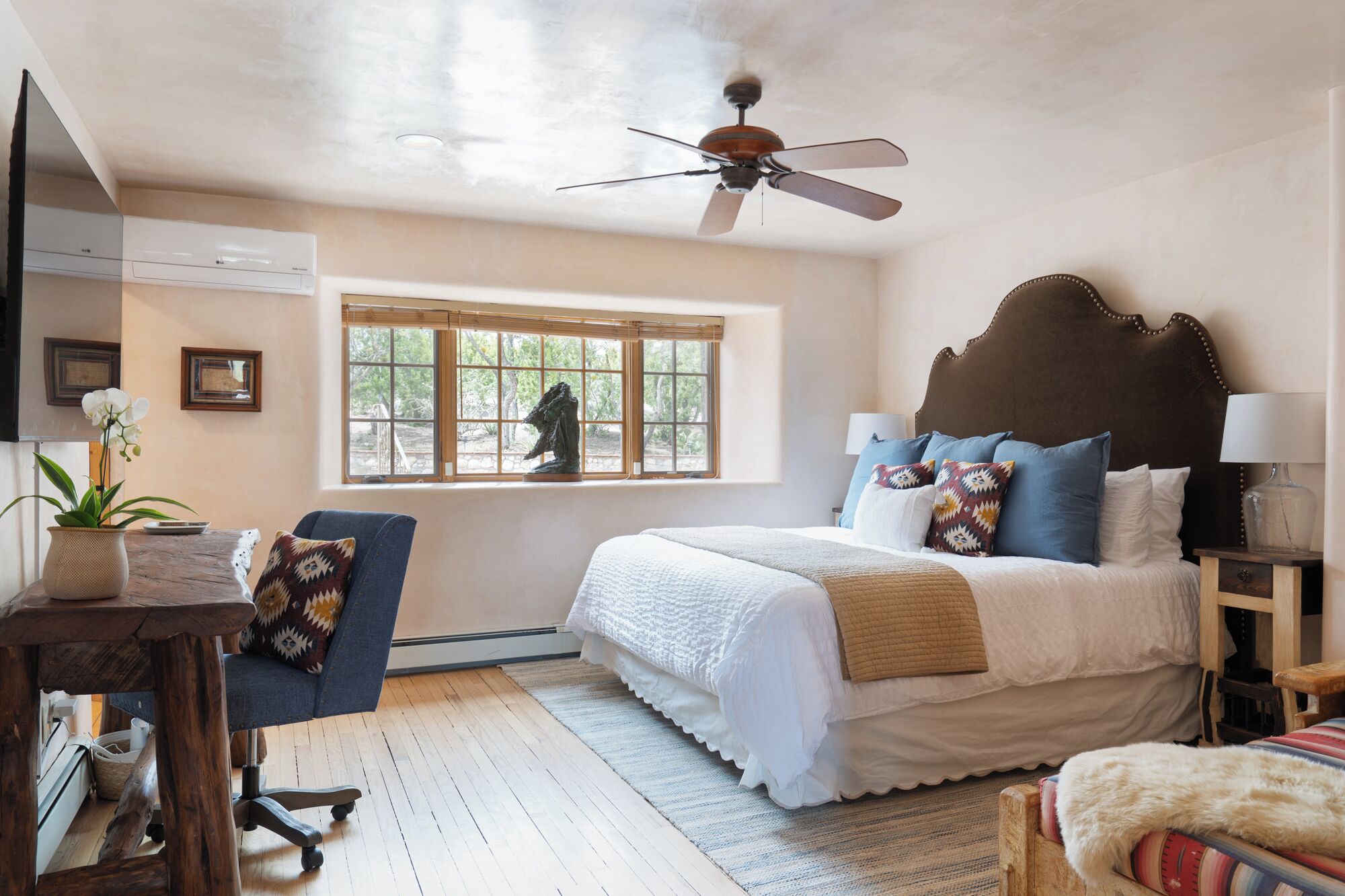 Un dormitorio con cama, ventilador de techo, ventana con vistas y escritorio con planta.
