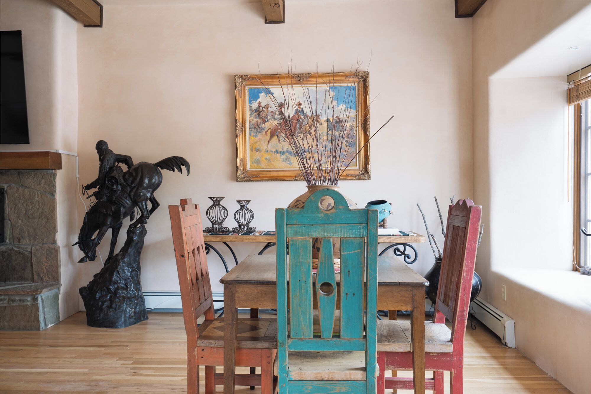 A dining area with a wooden table, chairs, a painting on the wall, and a statue.