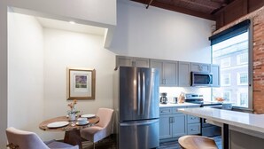 A modern kitchen with grey cabinets, a stainless steel refrigerator, and a window with a view of buildings. - Luxury Downtown Executive Loft @ the ABODES ApartHotel (Rochester)