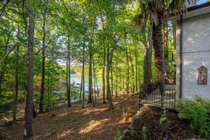 A forested area with a view of a lake, a dock, and a building with a brick wall and a balcony.