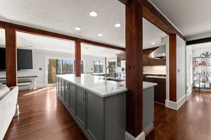 A spacious kitchen with a large island, wooden beams, and a view to the outdoors.
