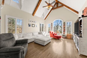 A spacious living room with a sectional sofa, a red armchair, and a dining area with a TV.