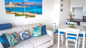 Een moderne woonkamer met een beige bank, blauwe en witte stoelen en een eettafel. Een groot kunstwerk toont een kustlandschap.
