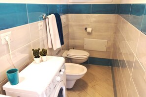 A compact bathroom with a washing machine, a toilet, and a small sink.