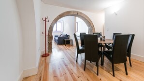 Zona de menjador amb arc de pedra, sòl de fusta i cadires negres.