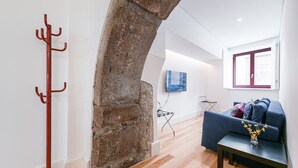 Un saló modern amb un arc de pedra, un penjallumbeigs vermell, un sofà blau i una televisió penjada a la paret.