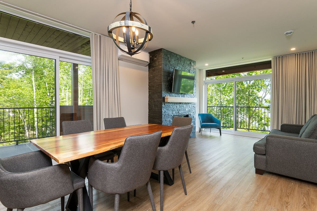 A spacious room with a large dining table, grey upholstered chairs, a blue sofa, and a stone fireplace.