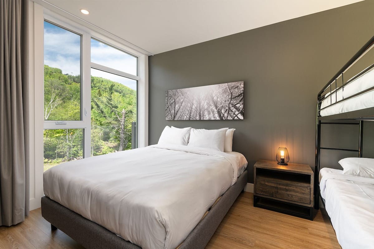 A modern bedroom with a large bed, a nightstand, a bedside lamp, and a bunk bed.