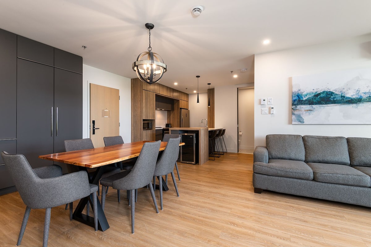 A modern kitchen with wooden cabinets, a central island, and a dining area with a wooden table and grey chairs.
