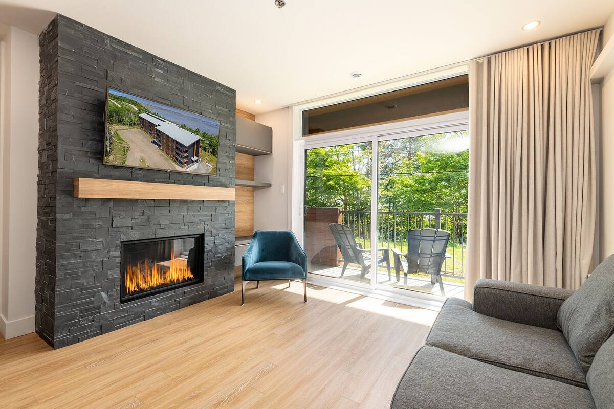 A modern living room with a stone fireplace, a comfortable sofa, and a glass door leading to an outdoor patio.
