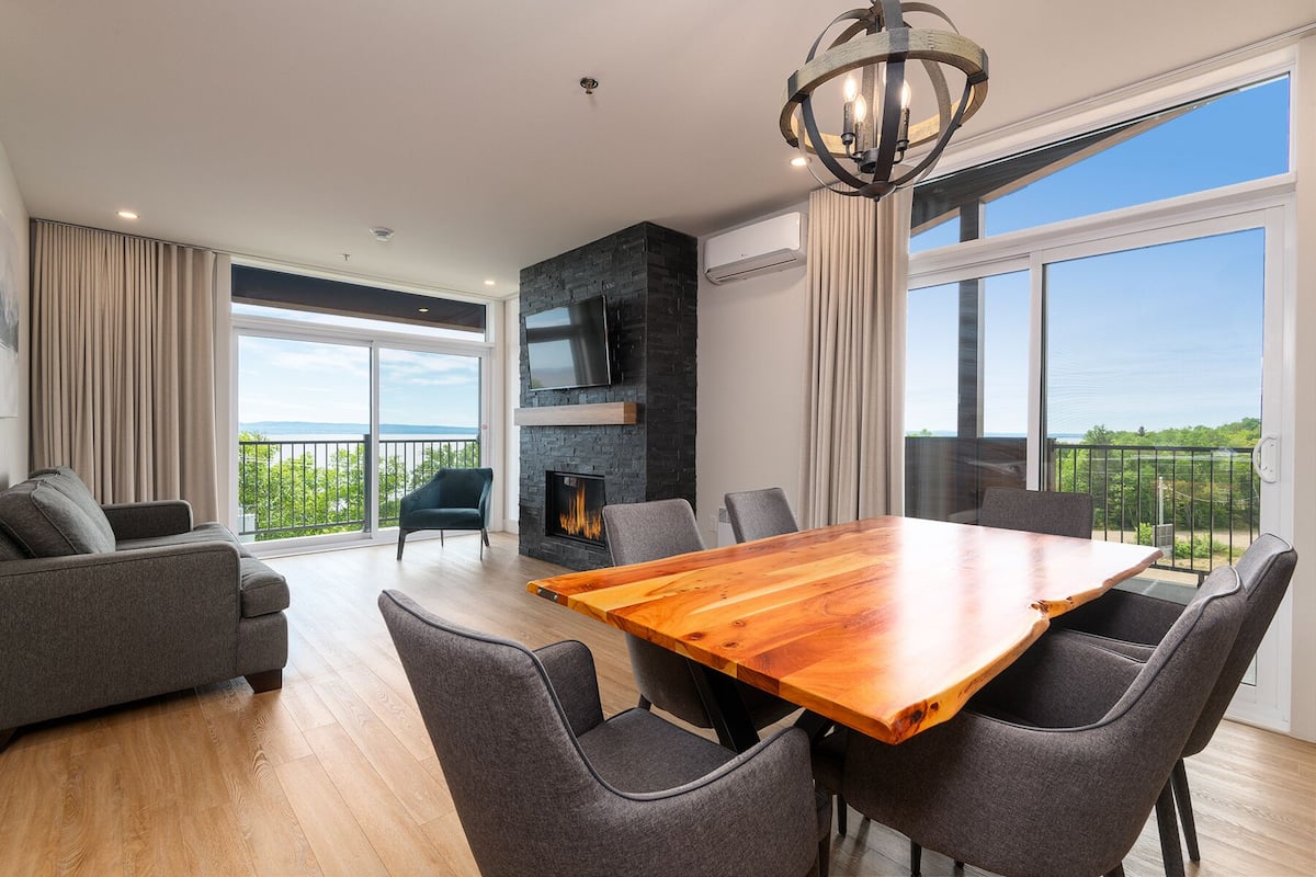 A modern living room with a large wooden table, grey sofas, and a fireplace.