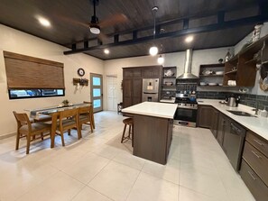 Uma cozinha moderna com armários de madeira escura, uma ilha central e uma área de jantar com cadeiras de madeira.