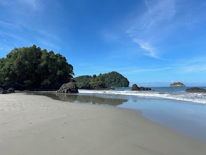 A beach with clear skies, calm waters, and rocky outcrops.
