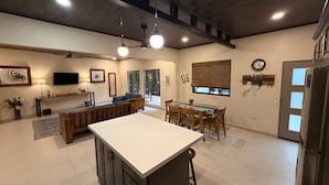 Una cucina moderna con isola centrale, zona pranzo e angolo soggiorno con divano e televisore.