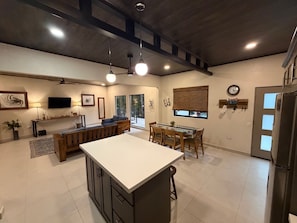 A modern kitchen with a central island, dining area, and a living space with a sofa and TV.