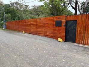 Uma cerca de madeira com uma porta preta, uma pequena placa preta e duas pedras amarelas no chão.