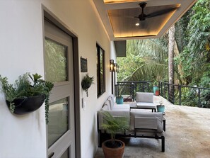 A modern outdoor seating area with a ceiling fan, potted plants, and a view of lush greenery.