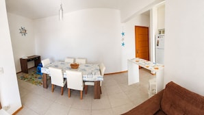 Un comedor con una mesa, sillas, una lámpara colgante, un reloj y un refrigerador al fondo.