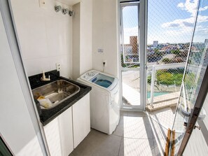 Eine kleine Küchenzeile mit Spüle und Waschmaschine, ein Balkon mit Blick auf die Stadt und eine Glastür zum Außenbereich.