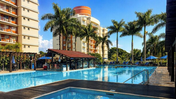Una piscina con cubierta de madera, rodeada de palmeras y un edificio de varios pisos con balcones.